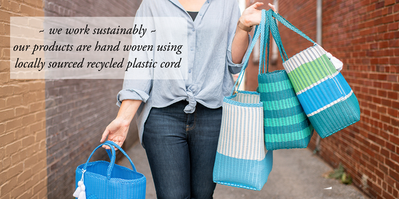 Sustainable recycled plastic handwoven tote bags. Guatemala artisan handmade. Locally designed in Maryland / DC. A collection of 4 totes in blues & greens held by person in alley. Text on image says 'we work sustainably ~ are products are hand woven using locally sourced recycled plastic cord'